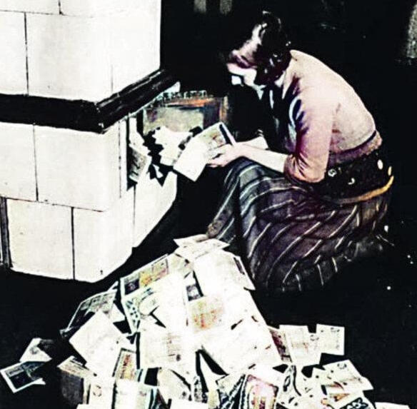 1923-24: A German woman feeds currency into a wood-burning stove because it burns longer than the firewood it could purchase.